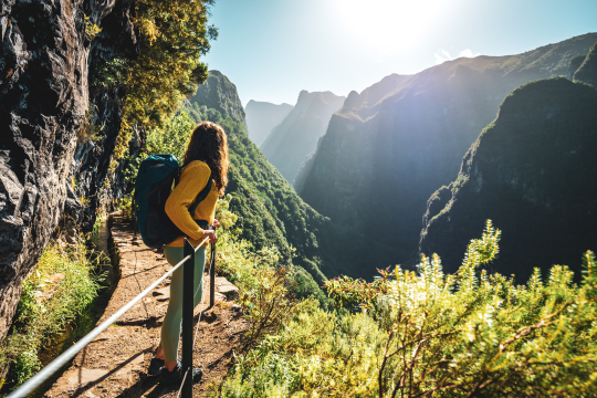 Frau mit Rucksack auf einem Wanderweg auf Madeira blick Richtung Horizont, rechts und links Berge